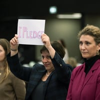 Three individuals stand together, one holds up a sign that reads 'I pledge'.