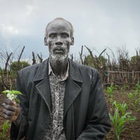 A South Sudanese man holds a plant in front of his field of crops