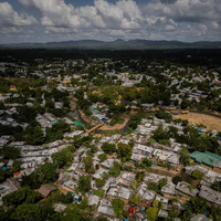 An aerial view of a huge refugee camp, trees throughout, with mountains in the background