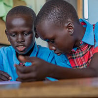 Two South Sudanese students sit together at a desk, concentrating on their work.