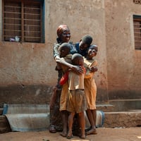 A Burundian woman hugs four of her children standing outside a building with a huge smile on her face