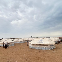 Refugee families gather with animals outside UNHCR tents in an arid environment