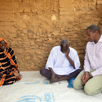 Mamadou Dian Balde sits on the floor, speaking with two Sudanese refugees.