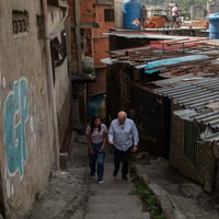 A man and a woman walk side by side up the staircase of a narrow street beside tin-roofed buildings 