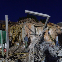 Two people assess damaged and collapsed buildings.