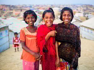 Three girls smile for the camera, in Kutupalong Refugee Camp.