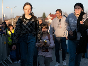 A woman and her daughters walk across the border between Ukraine and Poland carrying their belongings.