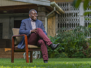 A smiling man sits on a chair in a garden