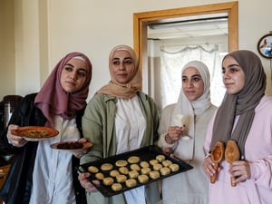 Quatre jeunes femmes portant un foulard tiennent un plateau de biscuits.
