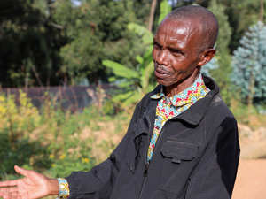A man stands in front of a nursery of tree seedlings in a refugee camp.