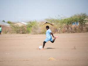 A girl prepares to kick a football on a dusty pitch.