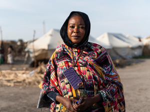 A woman in a colourful dress stands in front of rows of white tents in an IDP camp.