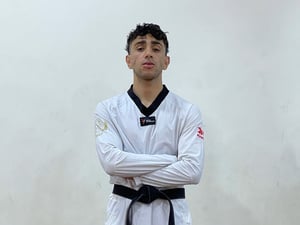 A man wears a white Taewkondo uniform with a black belt