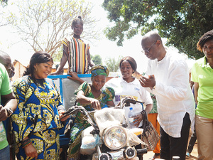 A group of people, smiling, gathers around a tricycle motorcycle