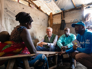 Personas conversan sentadas en un refugio provisional realizado con lonas de plástico y madera.