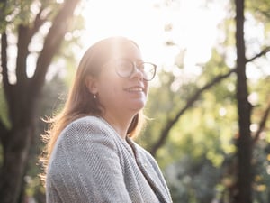 Sunlight shines through trees onto a woman wearing glasses and a business jacket 