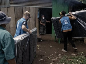 UNHCR staff deliver mattresses to a woman who stands in a doorway of a shelter.