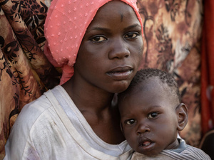 A young woman from South Sudan holds her one-year-old sister.