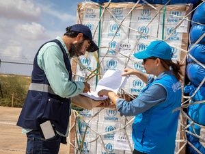 Two UNHCR staff members check a shipment of emergency supplies against a list