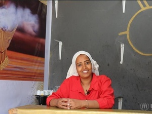 A woman wearing a bright red shirt stands behind the counter of a cafe