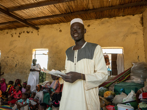 A young man holds some documents in a crowded room.