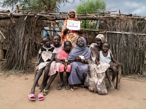 A family is pictured, smiling, in front of a shelter, with two members displaying their IDs.