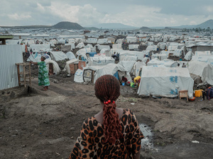 A rear view of a woman standing on muddy ground in front of hundreds of tents stretching to the horizon.