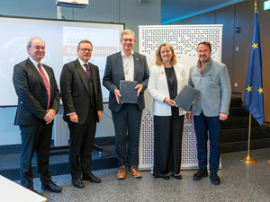 Four men and one woman stand looking at the camera while holding up two documents