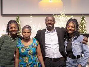 A pastor and his wife and two daughters pose for a photo in front of brightly coloured Chrismas tree.