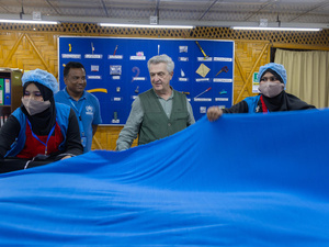 Four people stand holding a large blue piece of fabric in a production centre