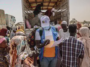 A UNHCR staff member checks documents in a group of people standing at the back of an open truck.