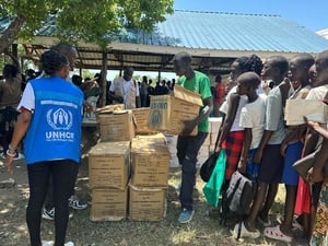Women and children line up to receive aid packages in boxes from a UNHCR staff member.