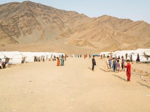 Tents line a dirt road where children gather, with a mountain in the background