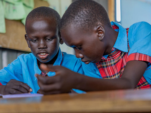 Two South Sudanese students sit together at a desk, concentrating on their work.
