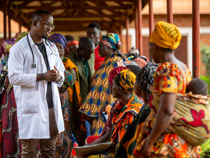 A clinician in a lab coat meets with a group of people outside.