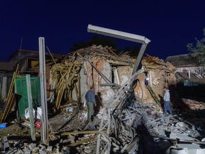 Two people assess damaged and collapsed buildings.