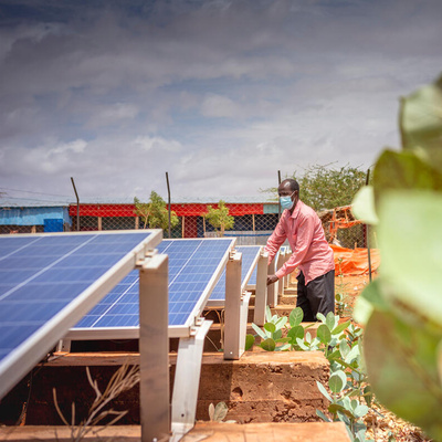A man stands next to a solar panel farm. 