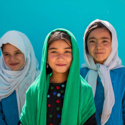 Three girls in colorful headscarves smile for the camera.