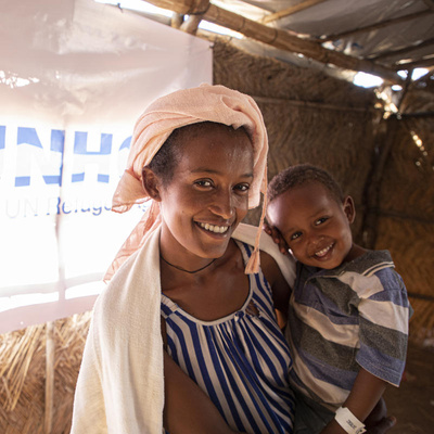 A mother holds her young son inside a UNHCR shelter. Both smile for the camera.