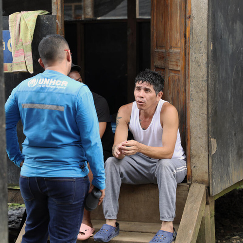 Owar, who fled Venezuela in search of a better life, sits on steps outside a shelter speaks with a UNHCR staff member.