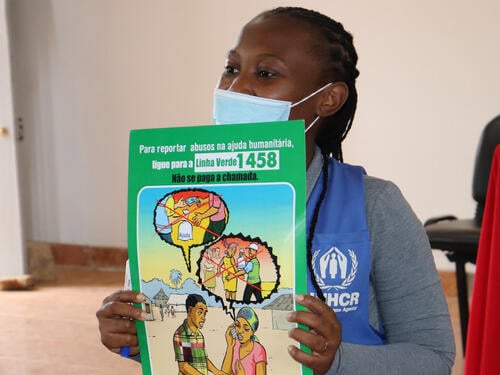 UNHCR personnel wearing a face mask holding up training resources in Spanish