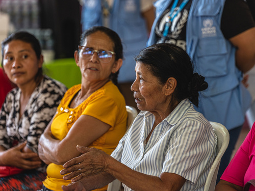 Several older people seated, in a discussion, with UNHCR staff behind them