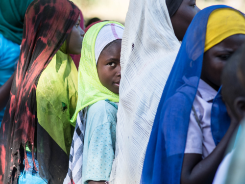 A young girl in a line of teenage girls turns and looks back at the camera.