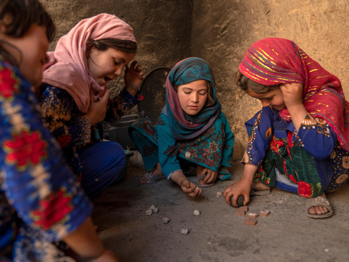 A small group of children play with rocks on the ground, Afghanistan
