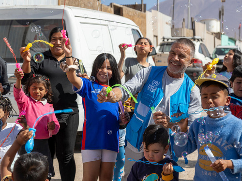 Osvaldo Laport blows bubbles with a group of smiling refugee, migrant and host community children and adults.