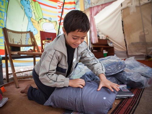 An Afghan boy opens a winter kit that will help him face harsh weather conditions in an open accommodation site