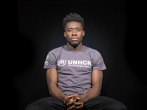 Alphonso Davies sitting in chair, wearing UNHCR t-shirt 