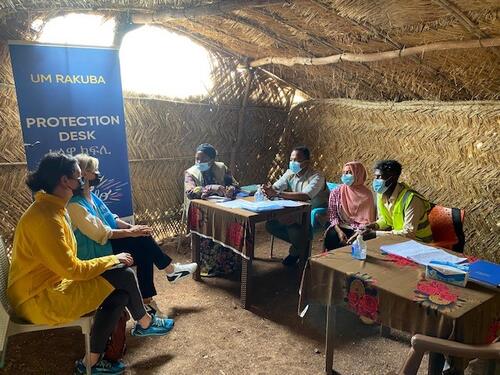 UNHCR staff members sit at a table and discuss with members of a local organization.