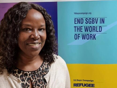 UNHCR former staff member Mildred stands in front of a UNHCR banner