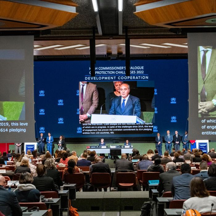 Three large screens show a projection of a speaker in a huge conference room.